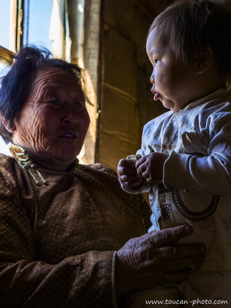 Enfant regardant par la fenêtre à la lumière du matin dans une maison en bois en Mongolie, avec sa grand-mère, scène de vie intergénérationnelle