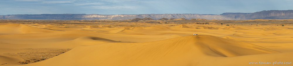 Homme touareg allongé sur une dune de sable du désert du Sahara en Algérie, se reposant sous la lumière chaude du soleil, paysage de dunes à perte de vue